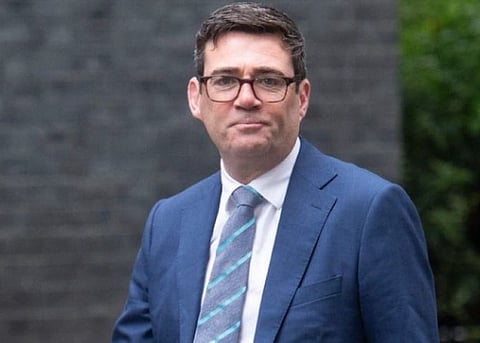 Image of UK's new PM Andy Burnham in a blue suit paired with blue but striped tie. he is seen walking and smiling at the camera. 