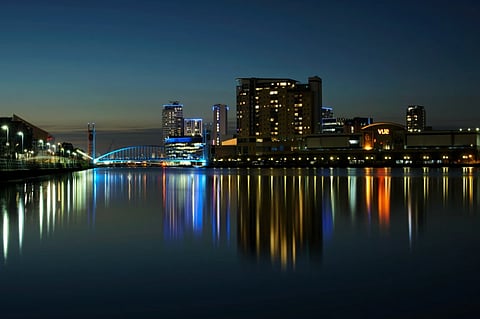 Nightscape of Salford Quays with illuminated buildings and water reflections in Manchester, England.