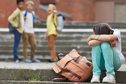 The image shows a child sitting covering her face and in background there are more children.