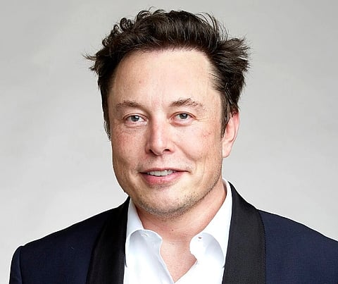 Image of  Elon Musk is a technology entrepreneur, investor, and engineer. in the image he is wearing a dark blue toned suit and is standing against a lighter background. 