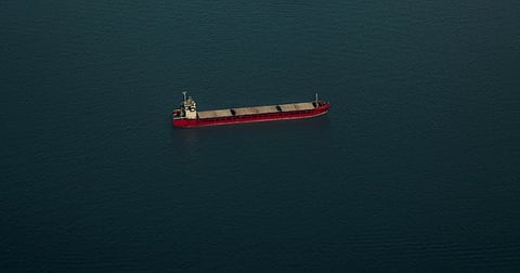 A lone cargo ship navigates the vast, serene expanse of the ocean under clear skies.
