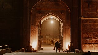 In the image two people are shown walking in the nigh-light of a monument from New Delhi, India