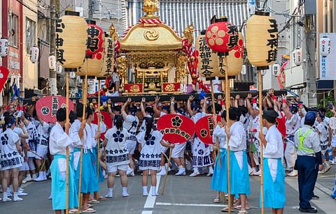 Vibrant scene of a traditional Japanese festival parade featuring participants carrying a Mikoshi through the streets.
