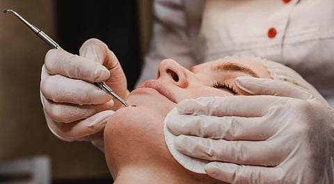 Image of a woman getting acne treatment at some fancy place. Another person seems to be removing the client's blackheads or dead skin cells.