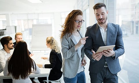 Image of two professional people discussing while  four people are discussing on the table/ 