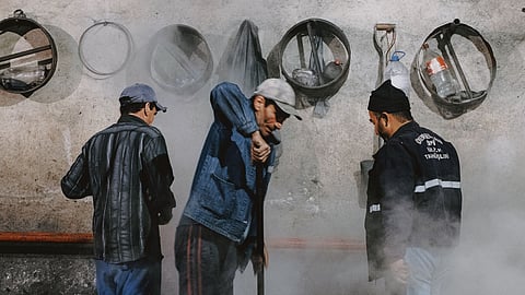 The image shows a group of workers amidst smoke and dust, working in an industry-setting.