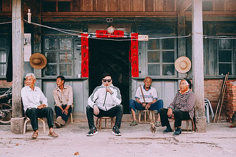 In the image a group of chinese people sitting outside a rustic building with traditional decorations, conveying community life.