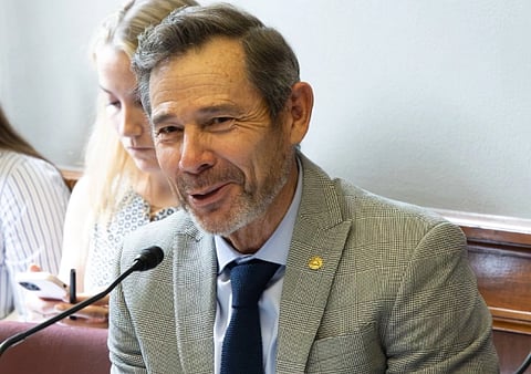 Image of US Senator John Curtis speaking in front of a mic in a room filled with people. 