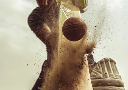 Cricketer in motion striking the ball with intense focus, clouds of dust captured.
