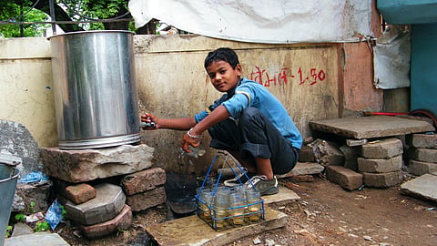 A child looking at the camera, washing the tea cups.