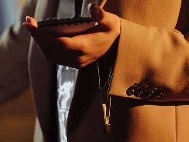 Close-up of a journalist holding a notepad and voice recorder, wearing a beige blazer.
