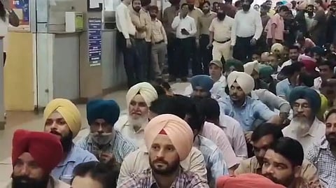 A group of men are gathered in a corridor. Some are sitting, while others stand at the rear.