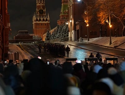 Crowds gather at Red Square under Spasskaya Tower lights on a winter evening.
