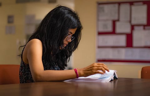 Focused young woman reading a textbook at a university library desk in New Delhi.
