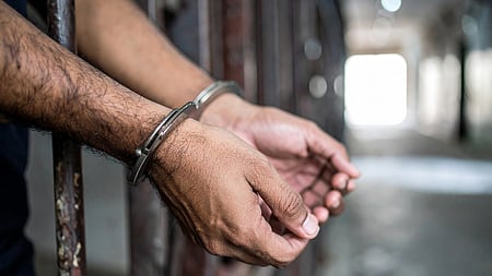 Image of man's hand behind prison bars and his hands are also cuffed 