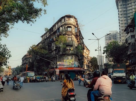 A lively street in Mumbai featuring scooters, old buildings, and urban life on a sunny day.
