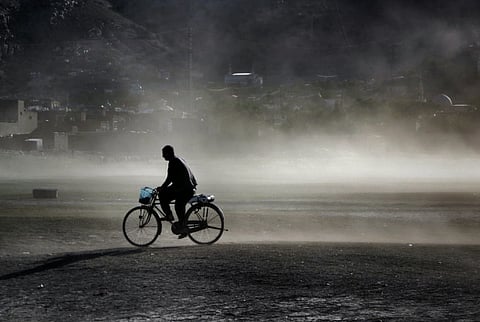 A lone cyclist rides through the foggy terrain in Kabul, Afghanistan, creating a dramatic silhouette.
