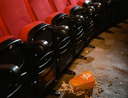 A movie theatre scene with spilled popcorn on the floor beside red seats. Captures the essence of cinema snacks.
