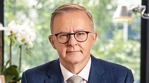 Image of Australian PM Anthony Albanese who is wearing a blue suit. In the background of the image which is blurred has flowers, a frame and a lamp light.