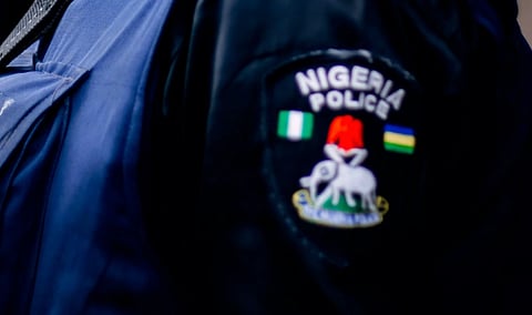 Close-up of a Nigerian police uniform showing an embroidered “Nigeria Police” badge, national flags, and crest against dark fabric.