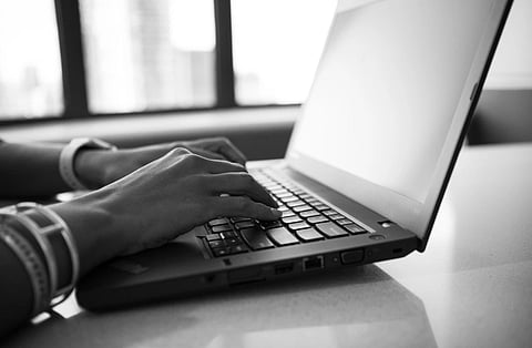 Close-up black and white photo showing hands typing on a laptop, emphasizing modern technology.
