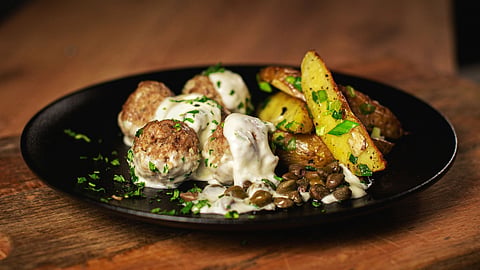 Image of Savory meatballs in creamy sauce with roasted potato wedges on wooden board.
