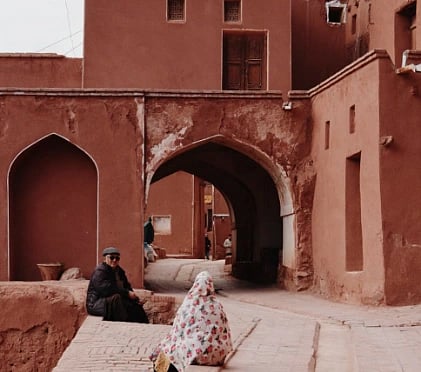 Image of the red architecture of Abyaneh village in Iran, showcasing traditional design with locals in view.
