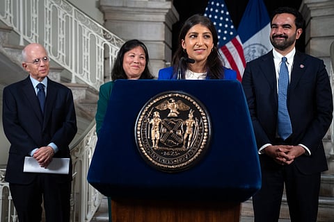 A woman standing on the podium speaking, while other stand in the background. 
