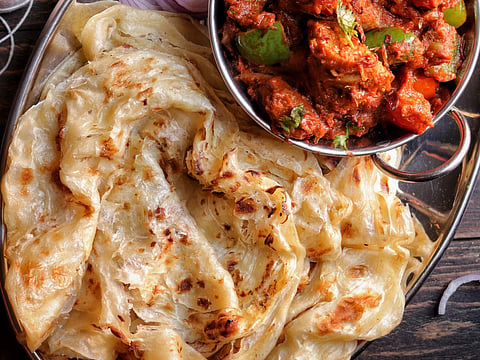 Close-up of Indian cuisine featuring paratha and spicy curry served with sliced onions.
