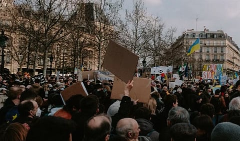 A bustling city protest with diverse activists holding flags and placards on a cloudy day.
