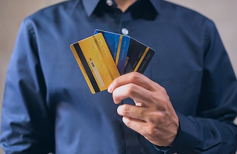 Person in a navy shirt fans out several credit cards in one hand, suggesting shopping, payment, or financial choices.