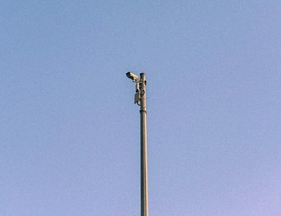 A CCTV camera mounted on a tall pole with a blue sky background in Dubai.
