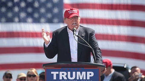 Donald Trump, wearing a red cap, speaks emphatically at a podium before a U.S. flag as a crowd watches at an Arizona rally.