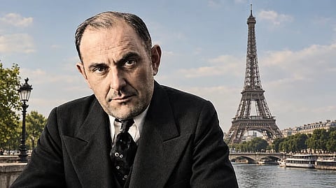 Serious man in a black suit and tie poses in the foreground beside Paris’s Seine River, with the Eiffel Tower behind him under a bright sky.
