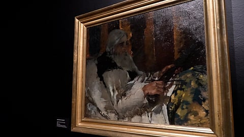 Framed impressionist painting of a bearded man in white clothing beside a colorful floral form, displayed against a dark museum wall.