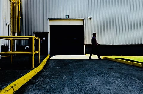 The image is of Person walking past a large industrial garage door in a daytime setting.
