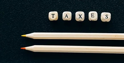 Wooden pencils on black background with tiles spelling 'TAXES'.
