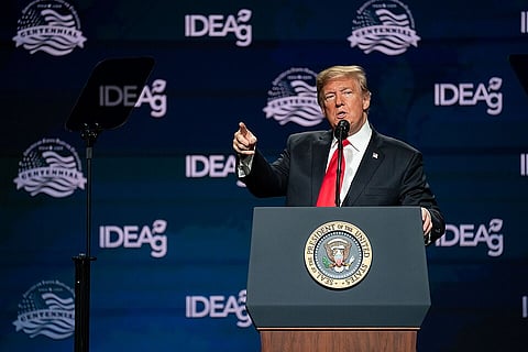 Donald Trump speaks and points from a presidential podium at an IDEA conference, against a dark blue logo backdrop; the formal, assertive scene is lit onstage.