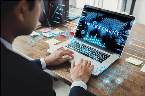 A business professional uses a laptop displaying investment charts and a world map, with glowing financial data overlays suggesting high-tech analysis.