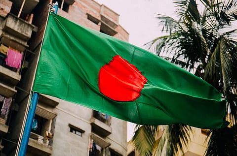 A vibrant Bangladesh flag waving against a cityscape backdrop, evoking patriotism.
