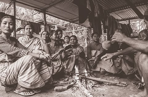 A tribal community gathered indoors in Assam. Captured in warm grayscale, it showcases their culture and traditions.
