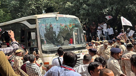 The image shows police officers detaining protesters, while a police bus carries the detainees to an undisclosed location.