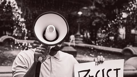 A protester holding a sign reading 'Resist' with a megaphone near a fountain outdoors.
