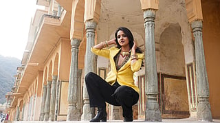 A stylish woman poses confidently in traditional Indian architectural surroundings.