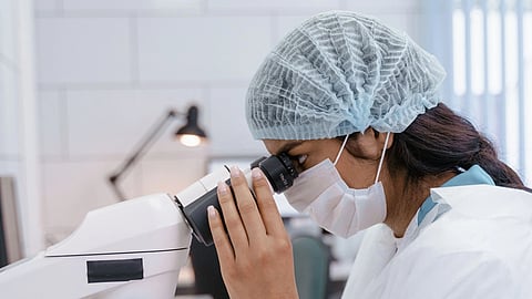Female scientist in lab coat using microscope for research in a laboratory setting.