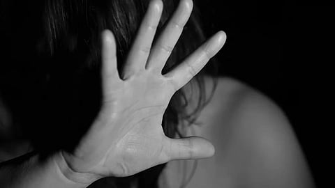 A black and white photo of a woman raising her hand, obscuring her face, suggesting a stop gesture.