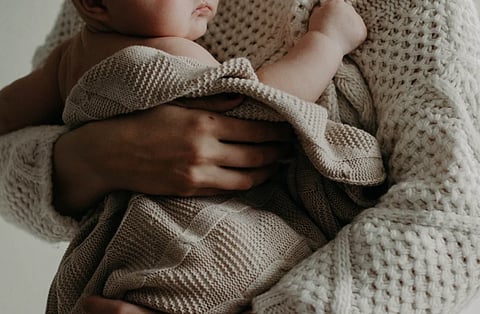 A tender moment of a mother holding her baby wrapped in a blanket, exuding warmth and care.

