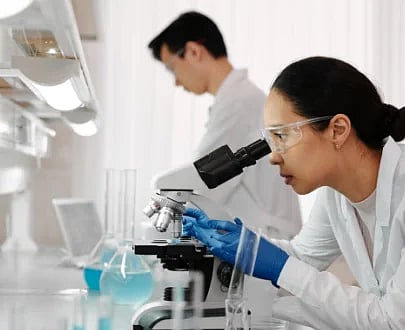 Researchers in a lab analyzing samples using microscopes and glassware.
