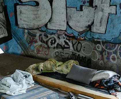 An urban scene depicting a makeshift shelter amidst street graffiti under a bridge.
