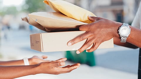 Close-up image of hands exchanging packages outdoors. Represents delivery and shipping services.
